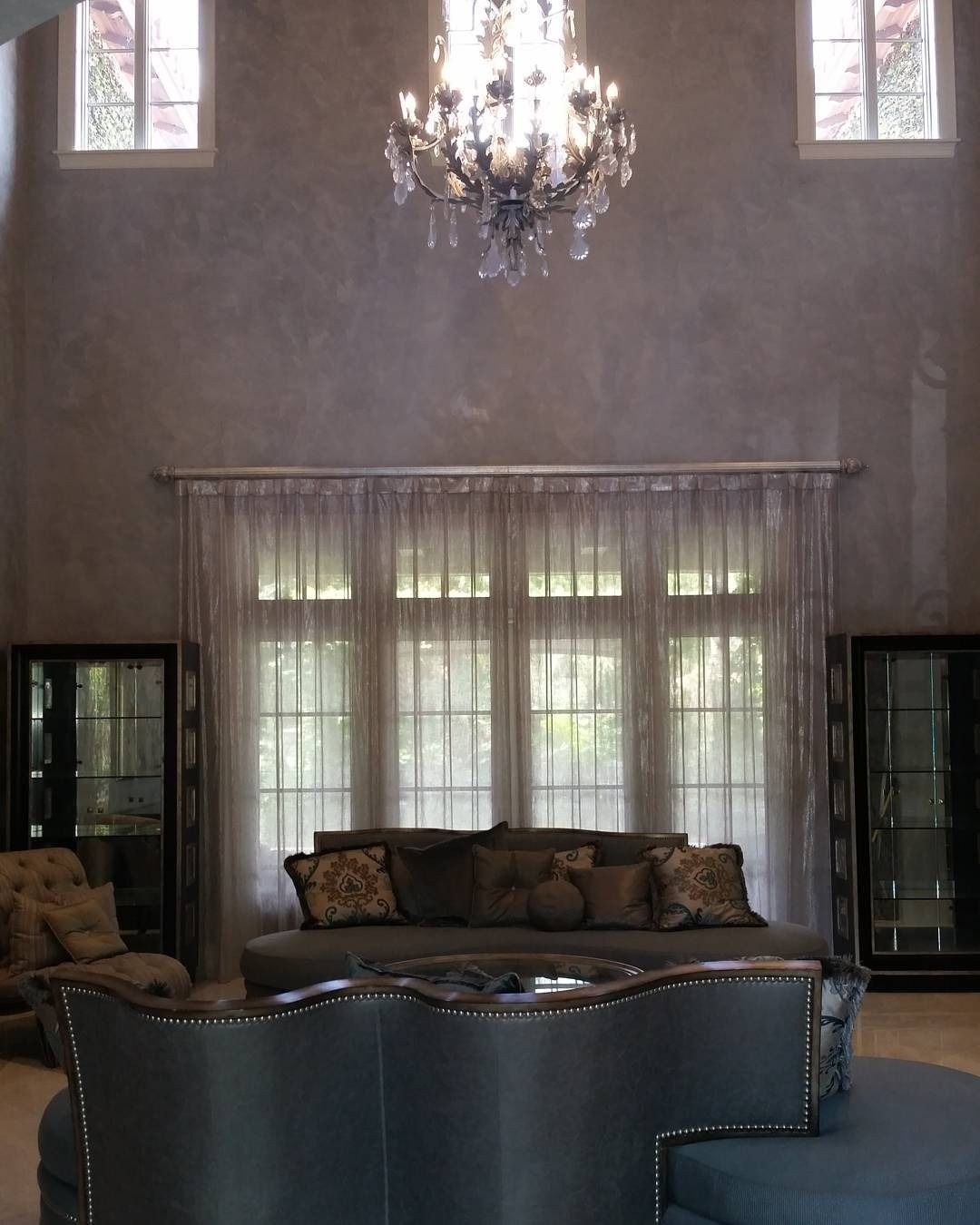 Living room with high ceilings, chandelier, sofa, windows, and neutral-toned walls.