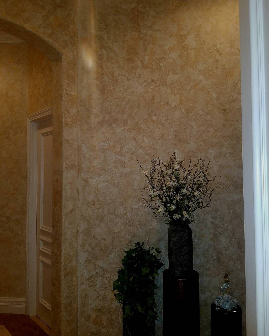 Textured beige walls with a floral arrangement, a small plant, and a doorway.