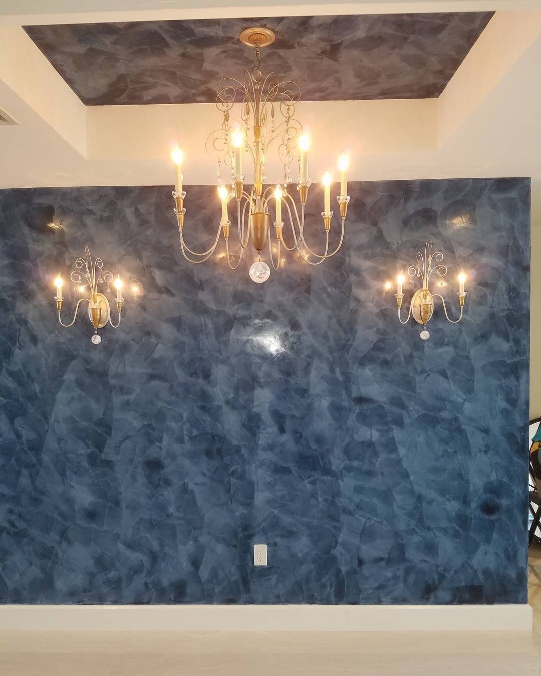 Dark blue textured wall with gold chandeliers and sconces in a room.