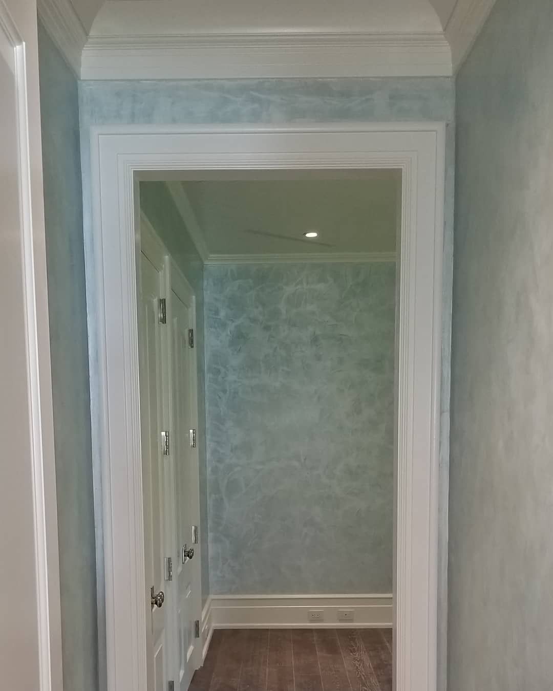 A doorway with white trim and aqua-colored textured walls. Brown floor visible.
