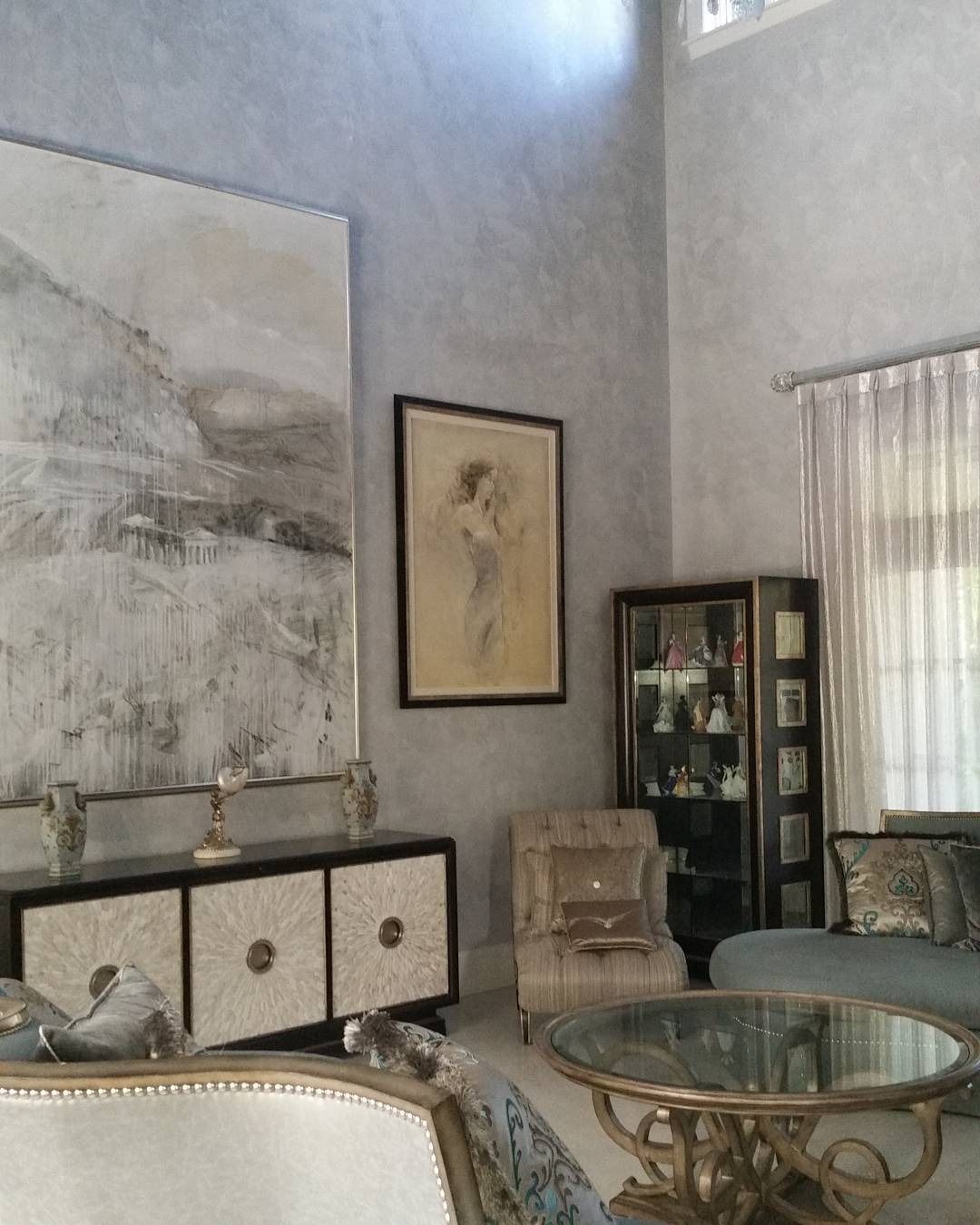 Living room with art, cabinet, chairs, and round glass table, mostly neutral colors.