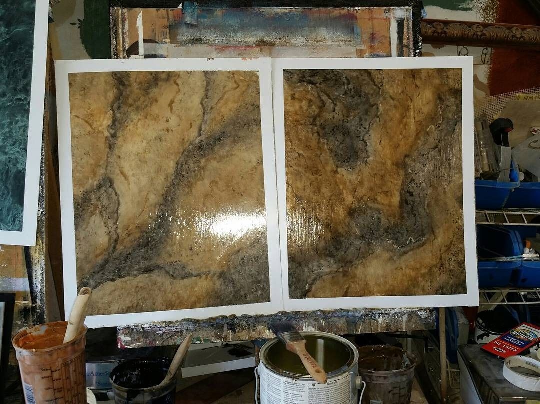 Two abstract paintings with marbled brown and black tones, drying in a studio.