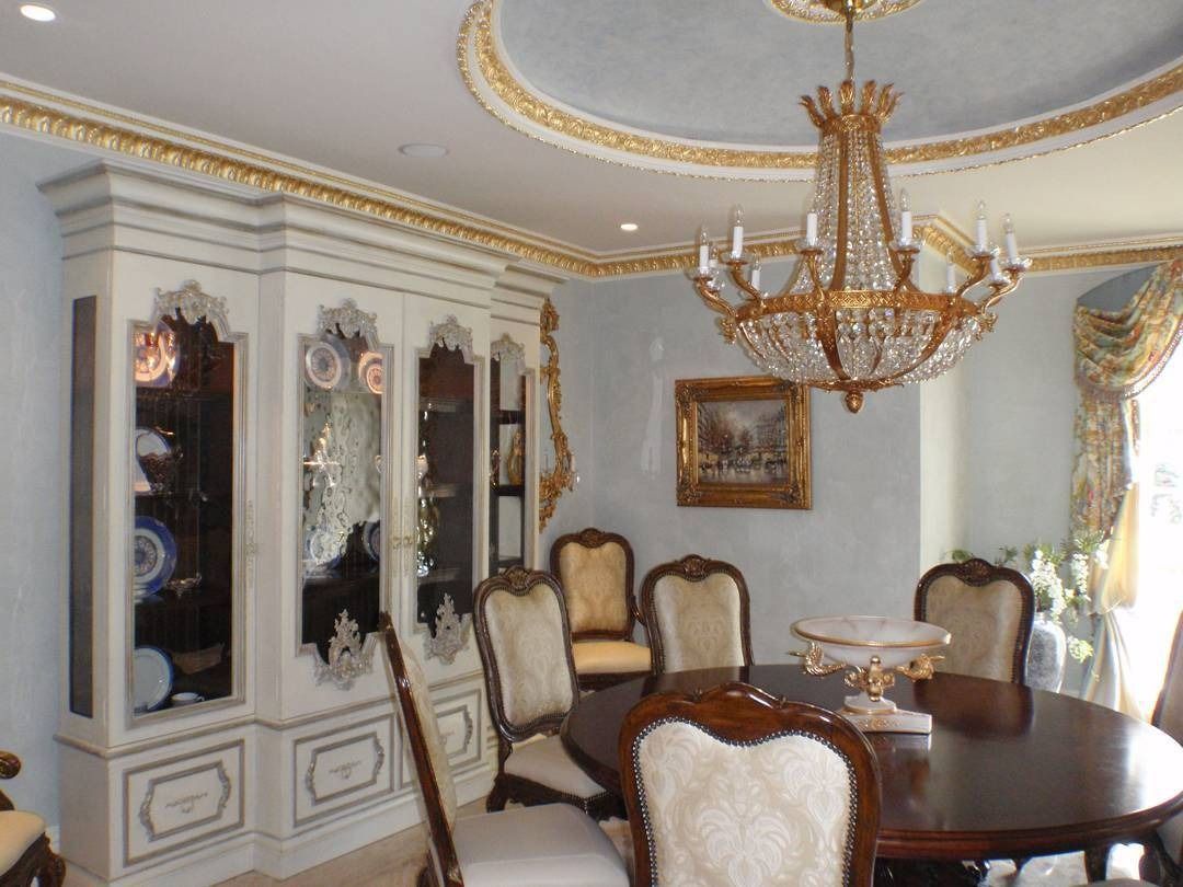 Ornate dining room with a large cabinet, chandelier, and oval table with chairs.