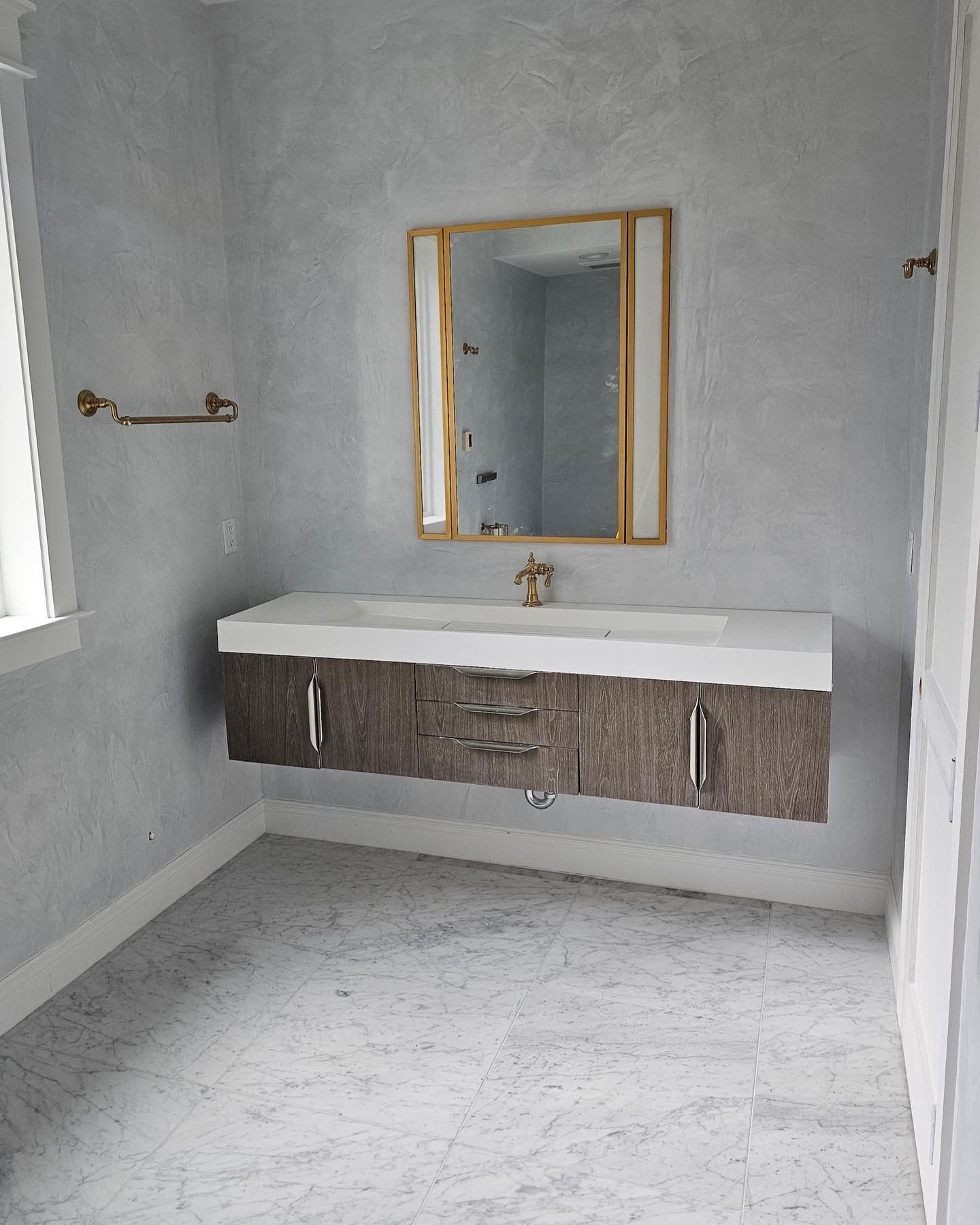Bathroom with floating vanity, gold accents, and gray walls and flooring.