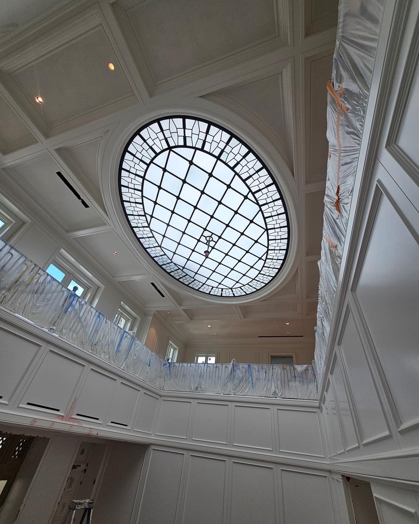 Interior view of a building with an oval stained glass skylight. White walls and trim.