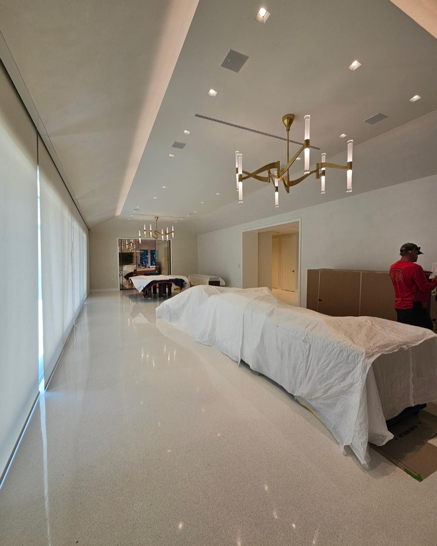 Large, bright white room with covered furniture. Man in red shirt stands near boxes.