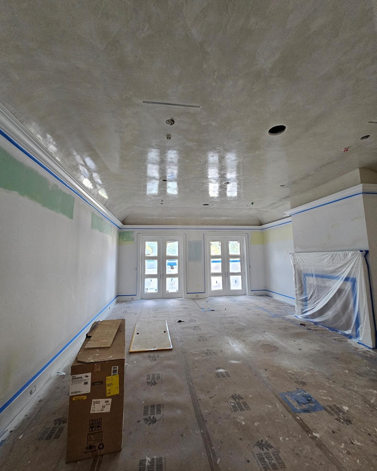 Interior of a room under construction with unfinished walls, ceiling, and doorways. Cardboard boxes are on the floor.