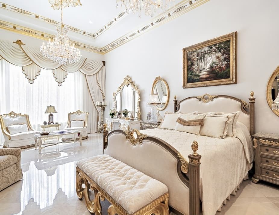 Luxurious bedroom with ornate gold and cream furniture, chandelier, and artwork.