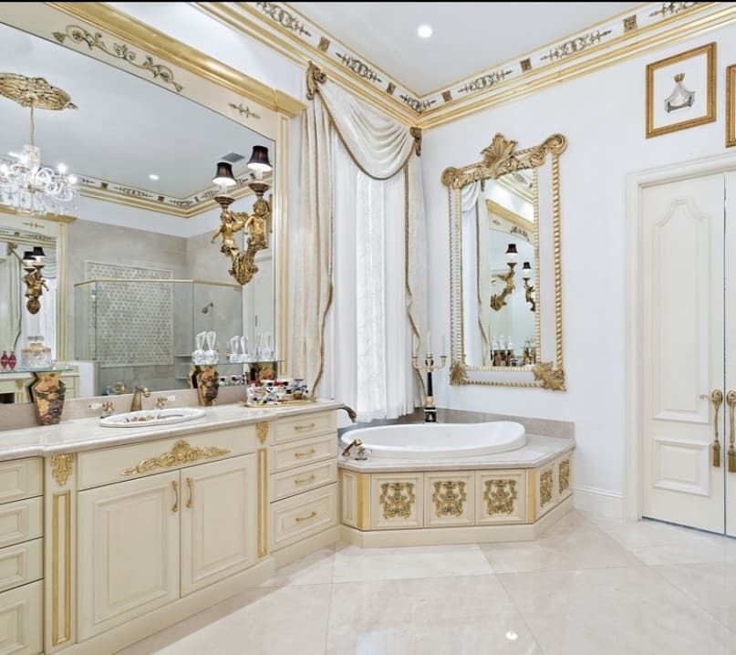 Ornate cream and gold bathroom with large mirrors, a tub, and detailed molding.