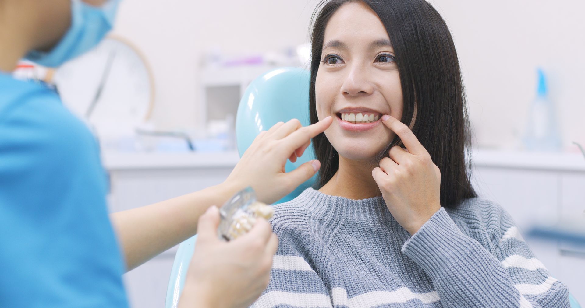 A dentist in blue scrubs shows a model of teeth to a smiling patient at a dental office.