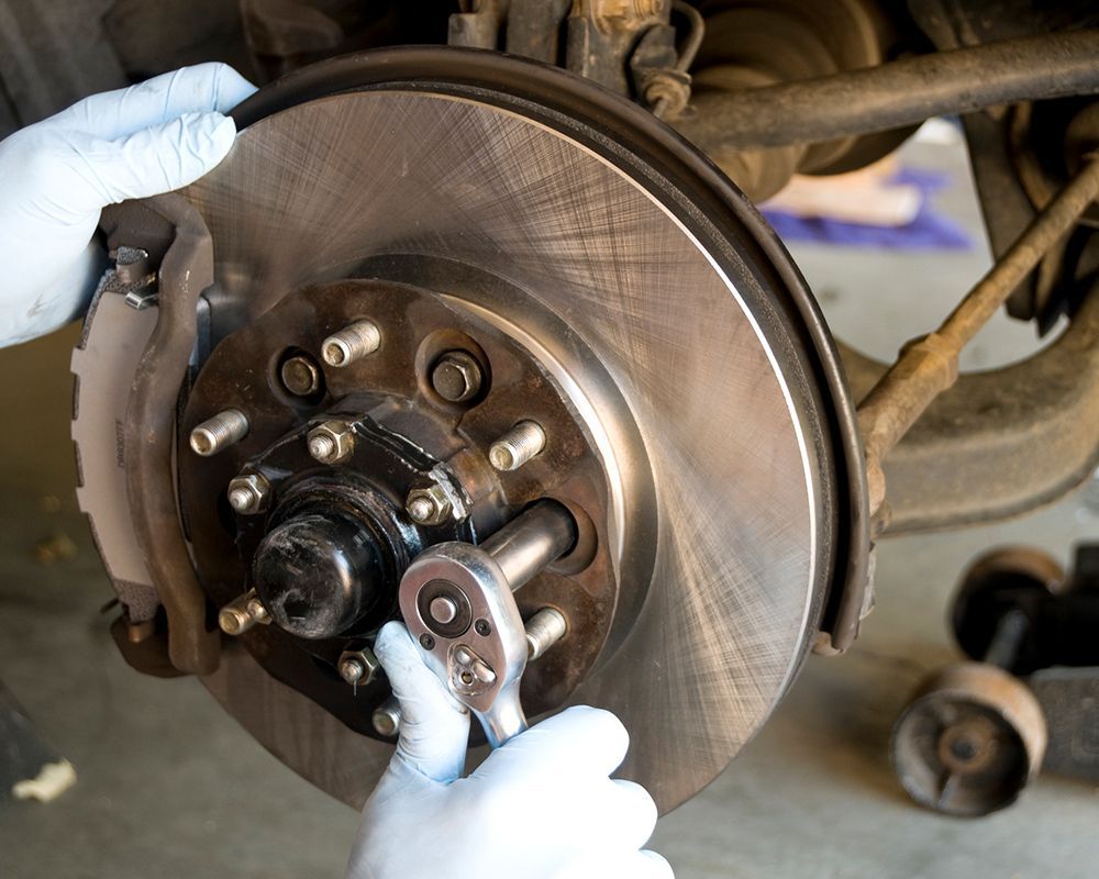 Mechanic at Bonita Point Auto Care performing car brake repair in San Diego, CA, using a ratchet to service the brake rotor.