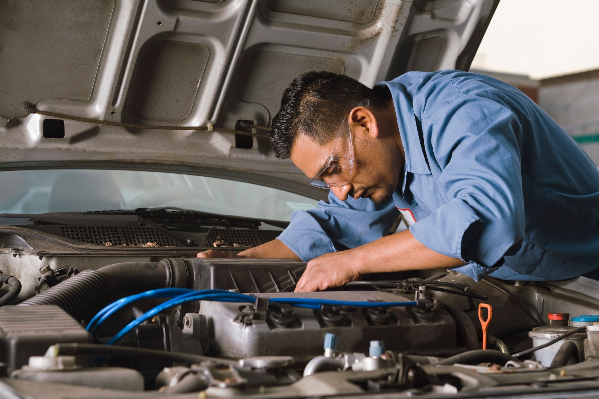 Auto mechanic in blue uniform repairing car engine under hood at professional vehicle service shop.