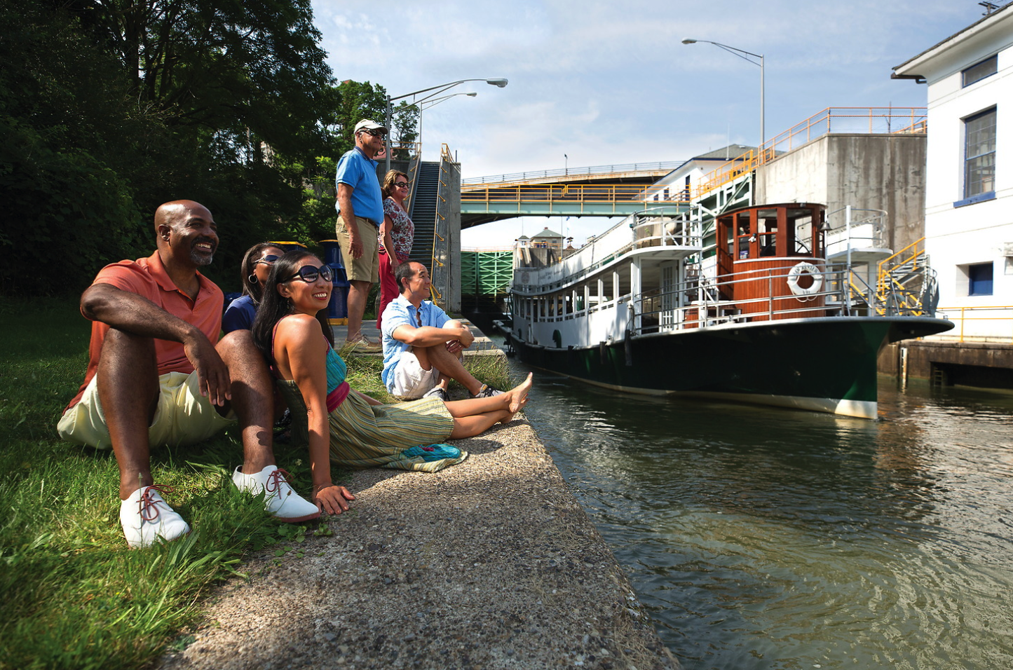 A group of people are sitting on the side of a river next to a boat.