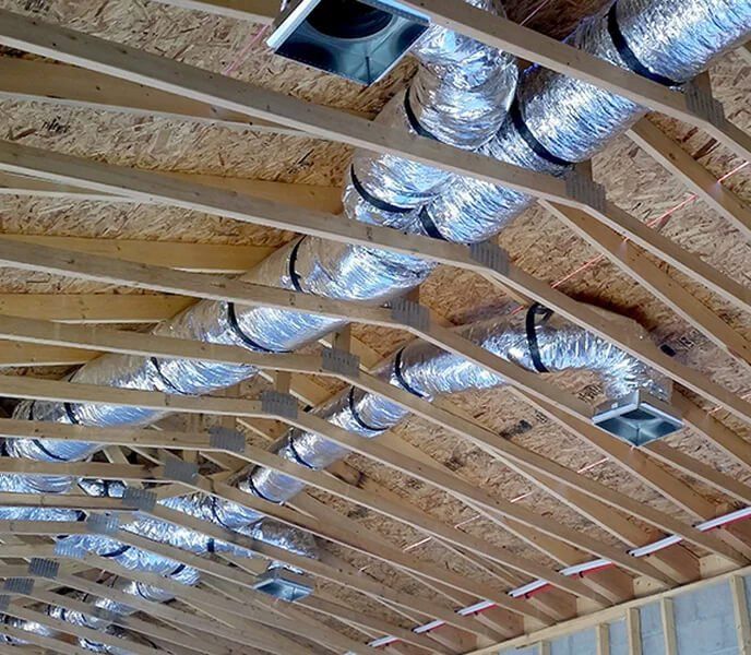 An installed air duct in an under-construction home supported by wooden frames.