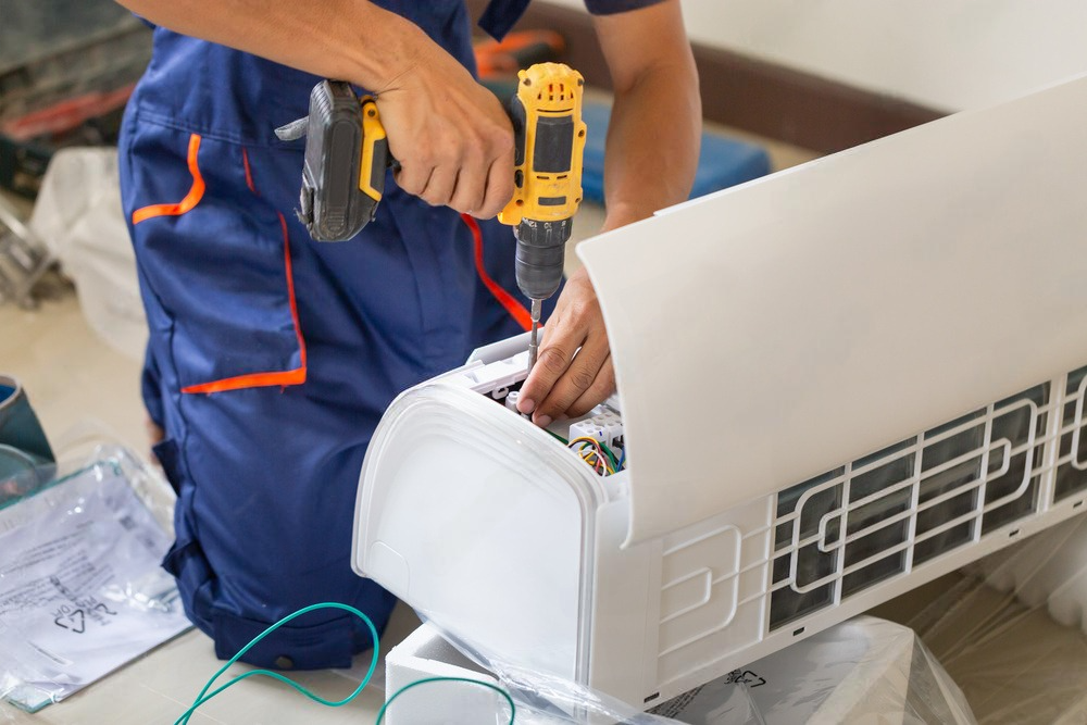 a man is fixing an air conditioner with a drill .