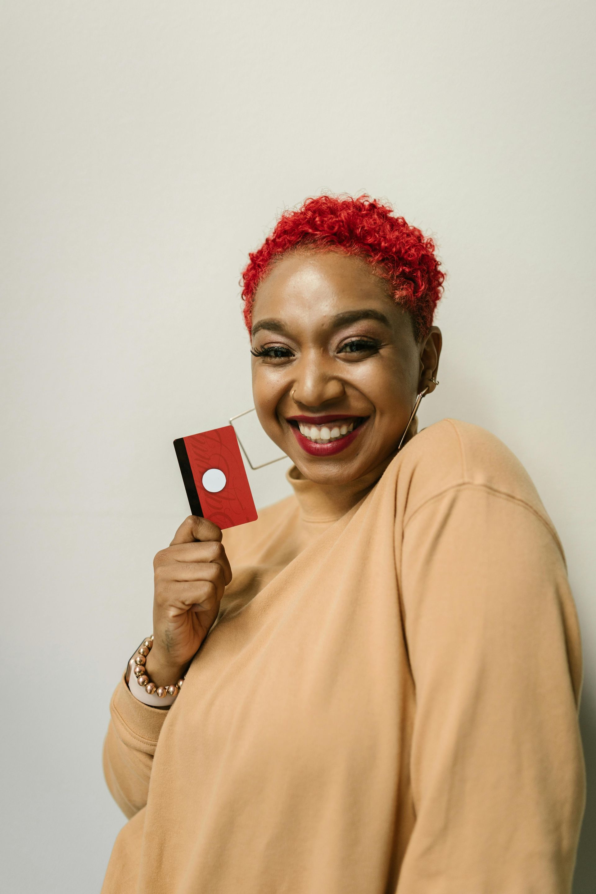 A woman with red hair is holding a credit card and smiling.