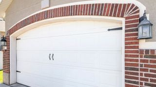 A white garage door is sitting next to a brick wall.