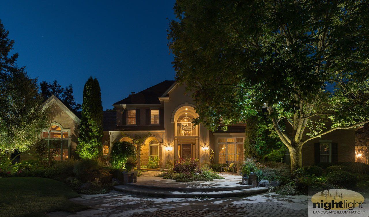 A large house is lit up at night with trees in front of it.