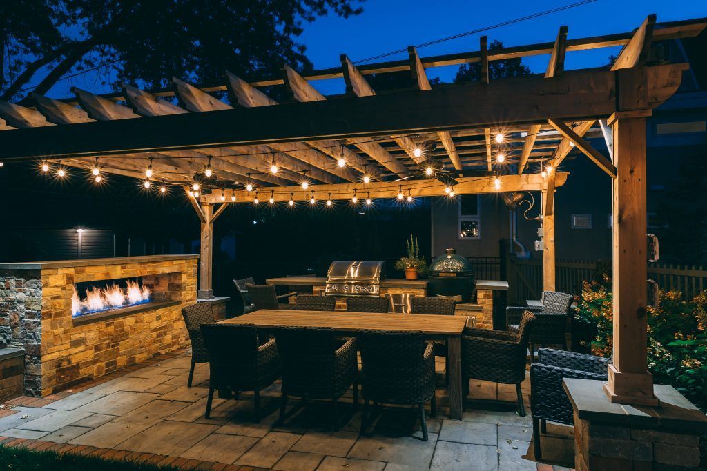 A patio with a table and chairs under a pergola at night.