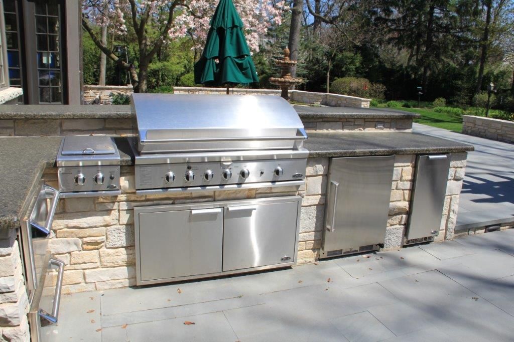 An outdoor kitchen with a stainless steel grill and a green umbrella