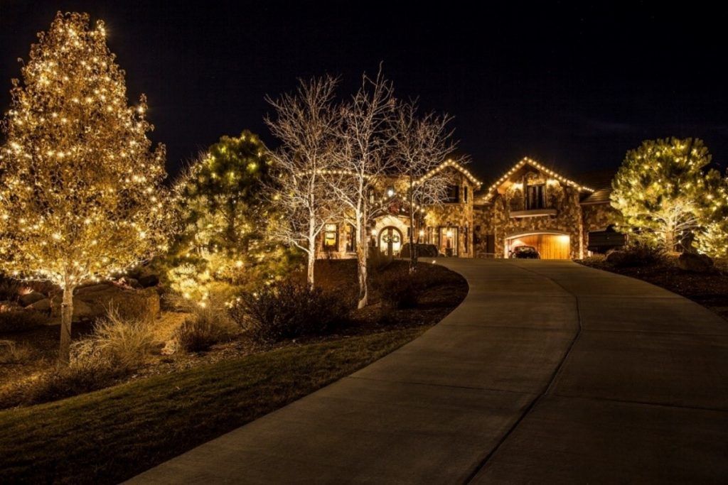 A house is decorated with christmas lights and trees are lit up at night.