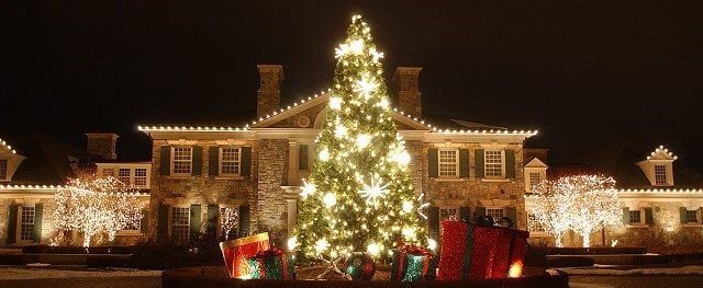 A large christmas tree is lit up in front of a large house.