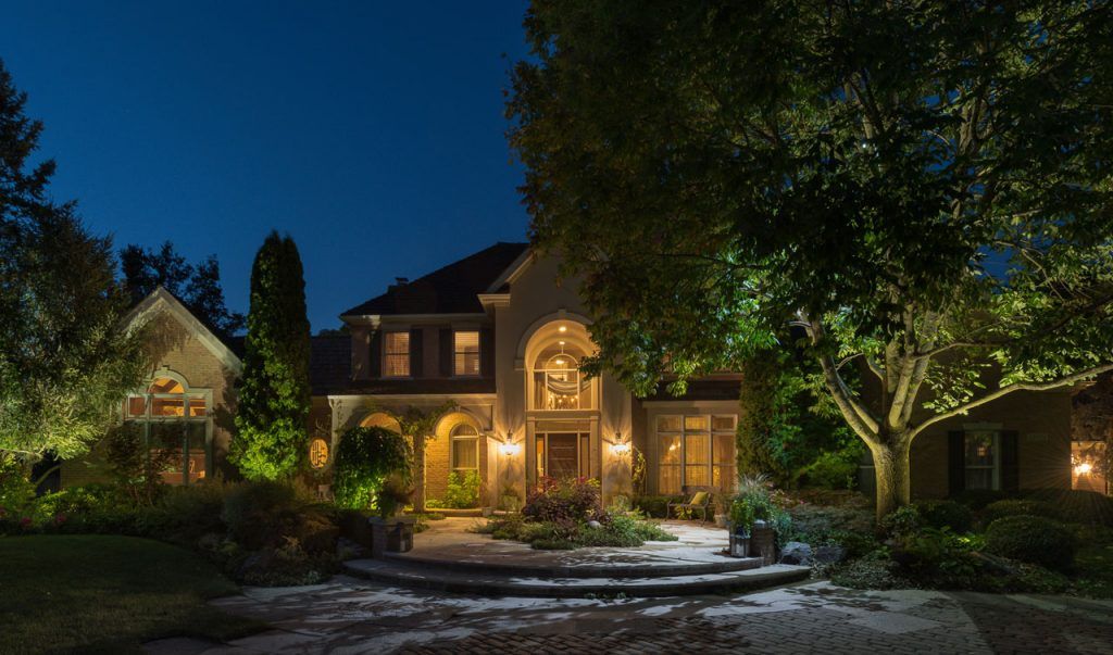 A large house is lit up at night with trees in front of it.