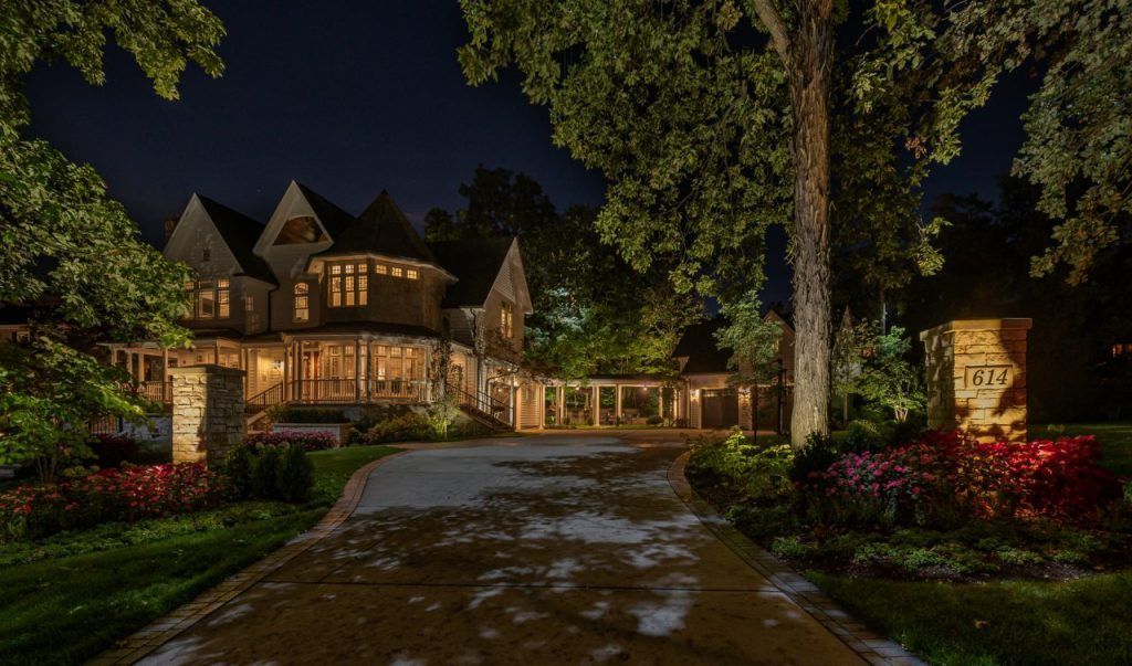 A large house with a driveway leading to it is lit up at night.