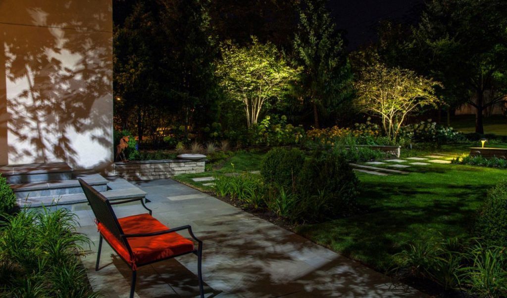 A bench is sitting on a sidewalk in a park at night.