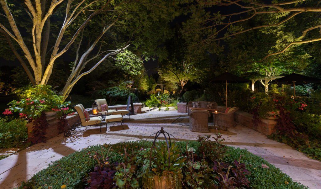 A patio area with a fountain and trees lit up at night.