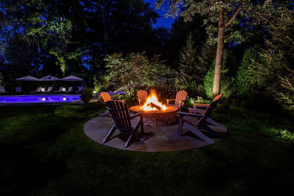 A fire pit with chairs around it in a backyard at night.