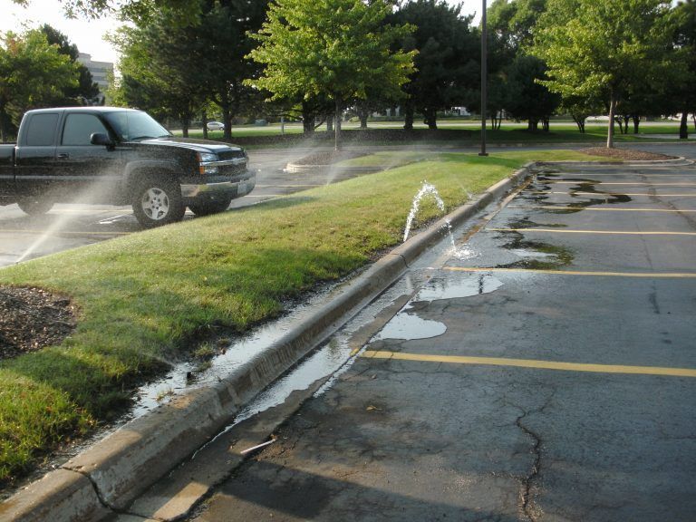 A truck is spraying water on the curb of a parking lot