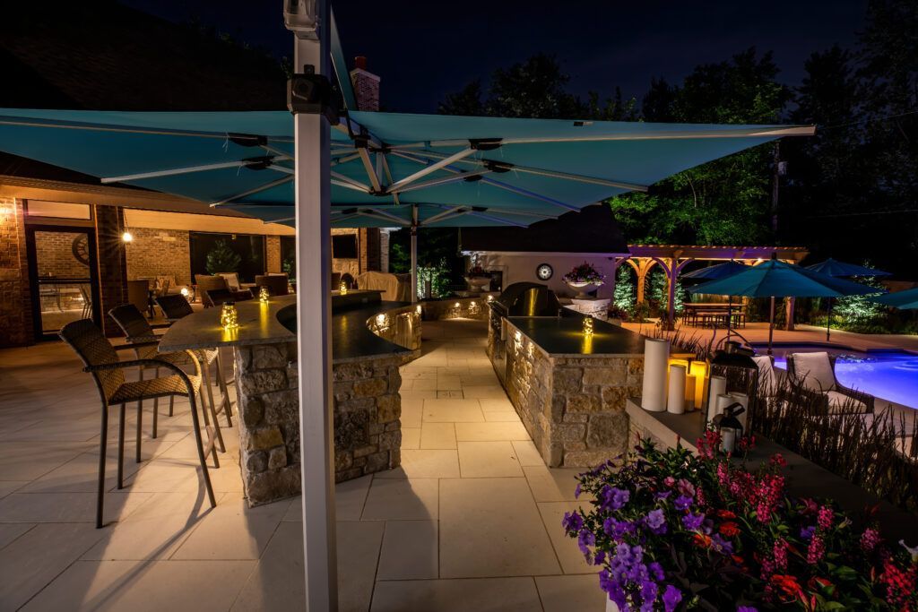 A patio area with umbrellas and a pool at night.