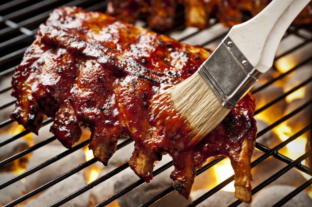 Ribs are being brushed with barbecue sauce on a grill.