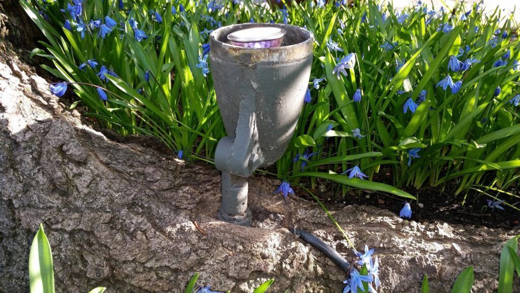 A lamp is sitting on a rock in a garden surrounded by flowers.