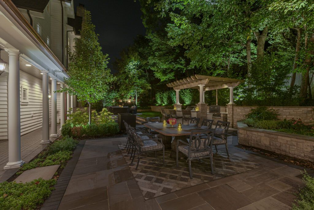 A patio with a table and chairs and a pergola at night.