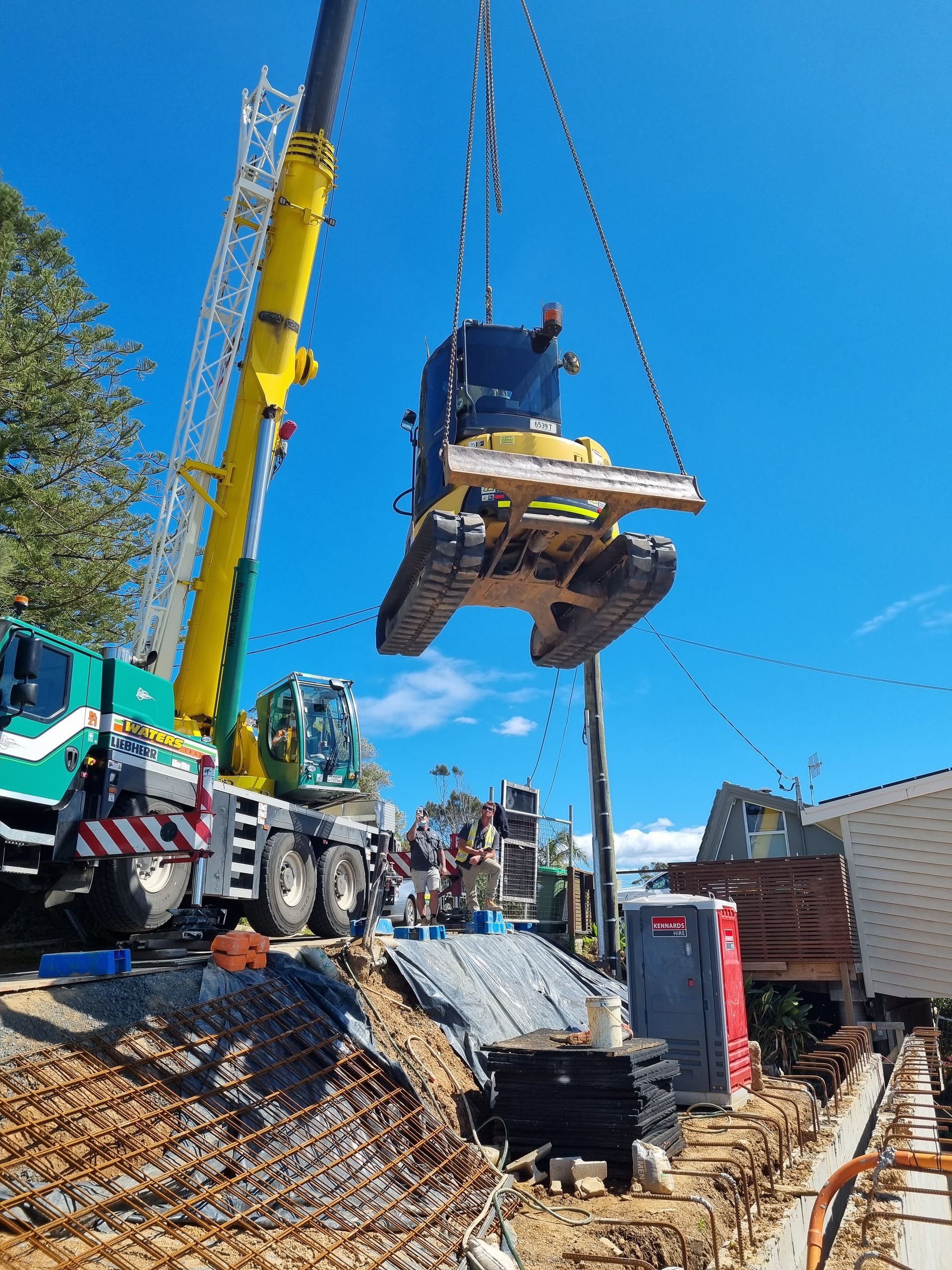 A crane is lifting a bulldozer into the air at a construction site. — Adam Lowe Earthmoving Pty Ltd in Somersby, NSW