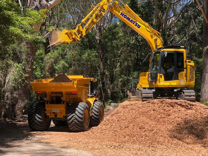 A yellow excavator is loading dirt into a dump truck. — Adam Lowe Earthmoving Pty Ltd in Somersby, NSW