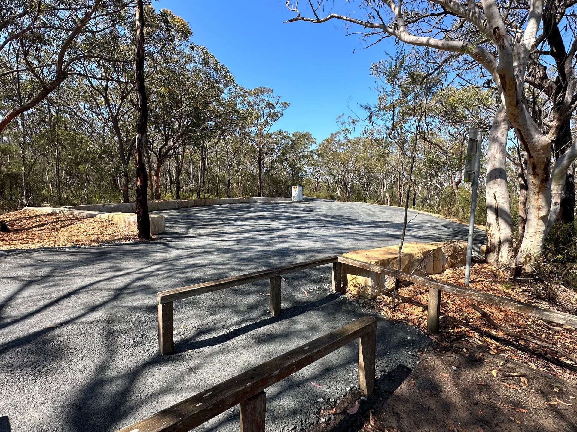 A wooden bench is sitting on the side of a road in the middle of a forest. — Adam Lowe Earthmoving Pty Ltd in Somersby, NSW