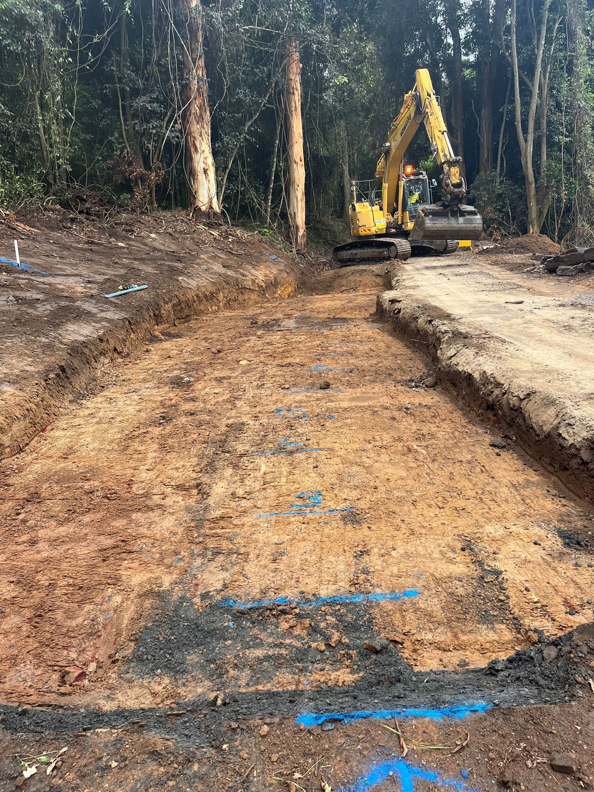 A yellow excavator is working on a dirt road in the woods. — Adam Lowe Earthmoving Pty Ltd in Somersby, NSW