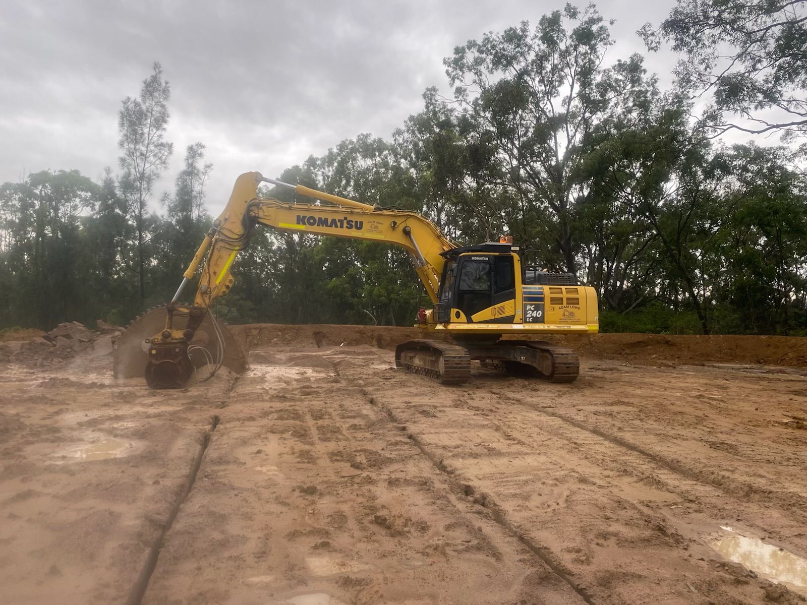 A yellow excavator is moving dirt in a muddy field. — Adam Lowe Earthmoving Pty Ltd in Somersby, NSW