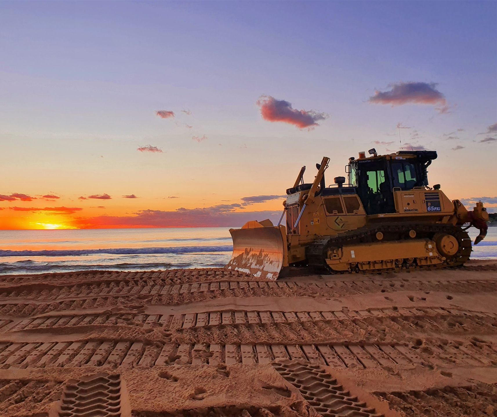 A bulldozer is sitting on the beach at sunset. — Adam Lowe Earthmoving Pty Ltd in Somersby, NSW