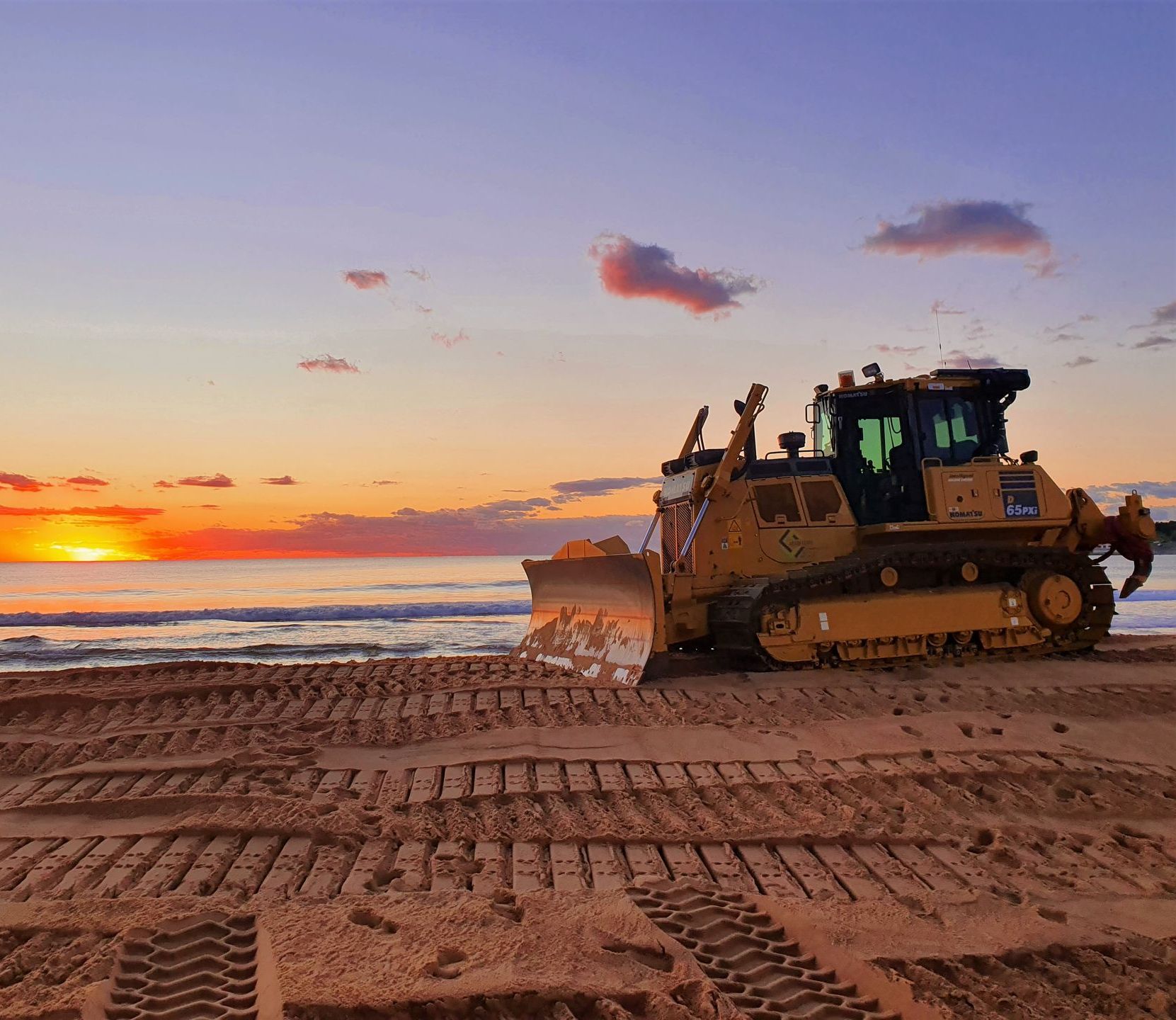 A bulldozer is working on a beach at sunset. — Adam Lowe Earthmoving Pty Ltd in Somersby, NSW