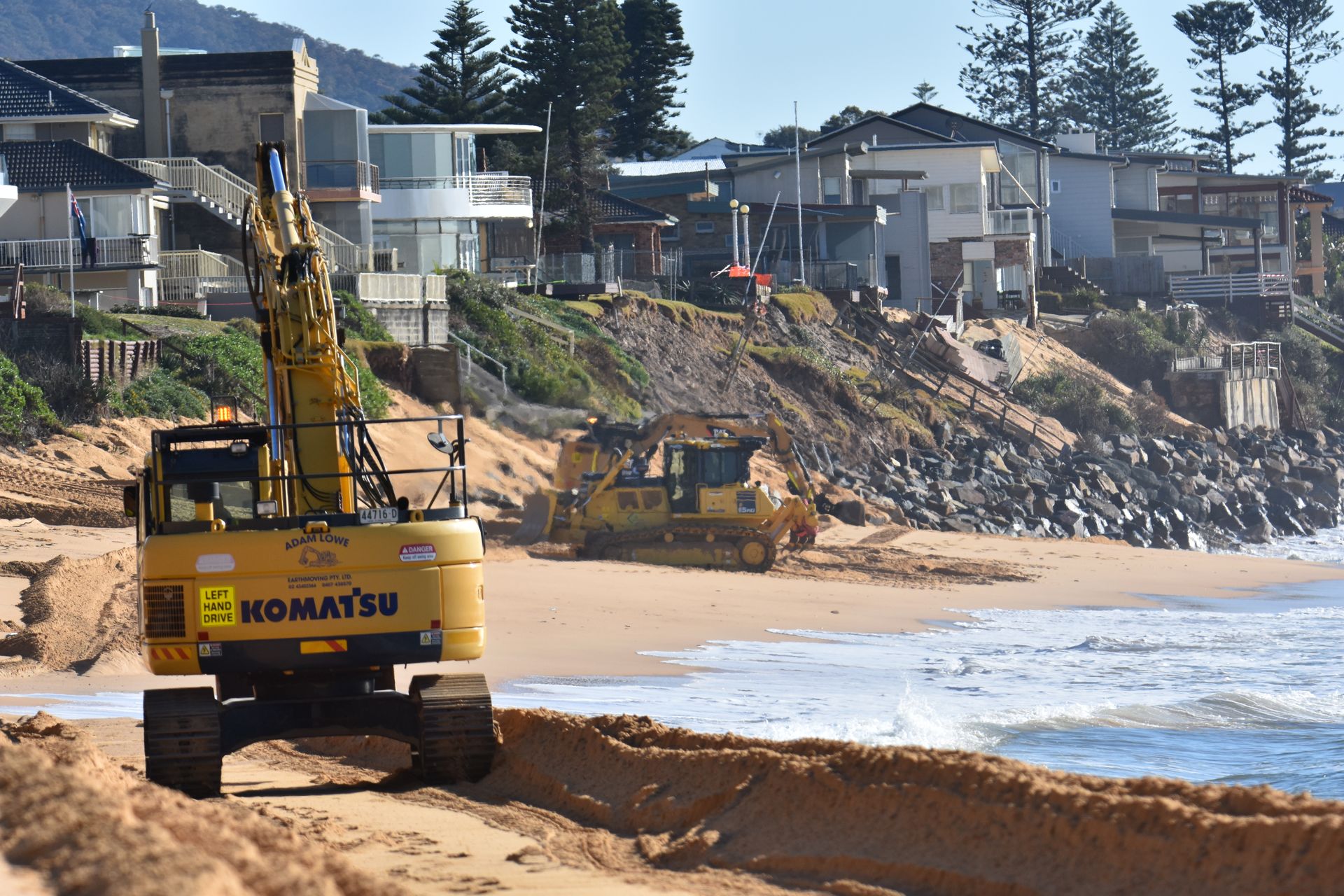 A yellow komatsu excavator is working on a beach. — Adam Lowe Earthmoving Pty Ltd in Somersby, NSW
