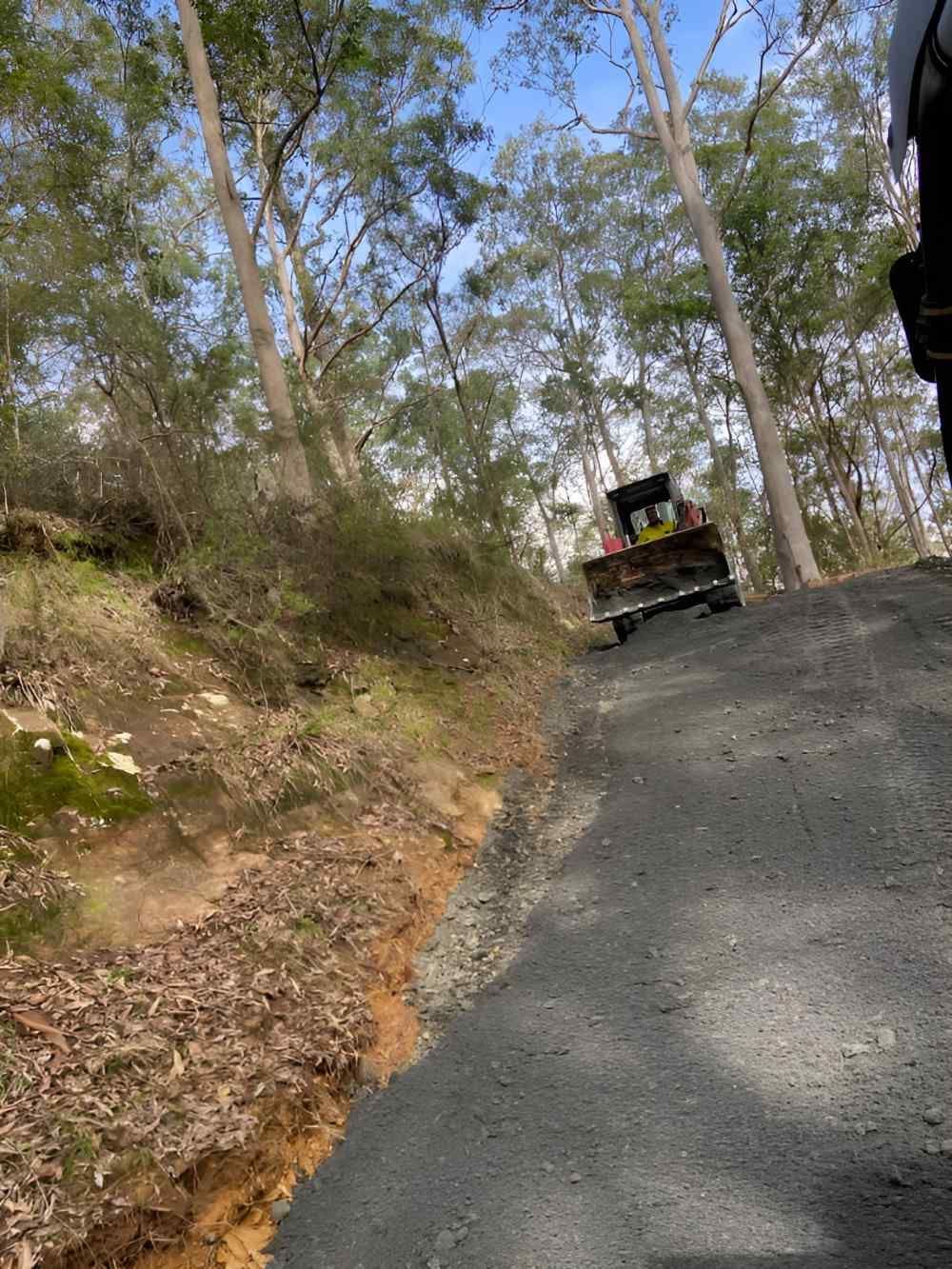 A Bulldozer Is Driving Down a Dirt Road in The Woods — Adam Lowe Earthmoving Pty Ltd in Somersby, NSW