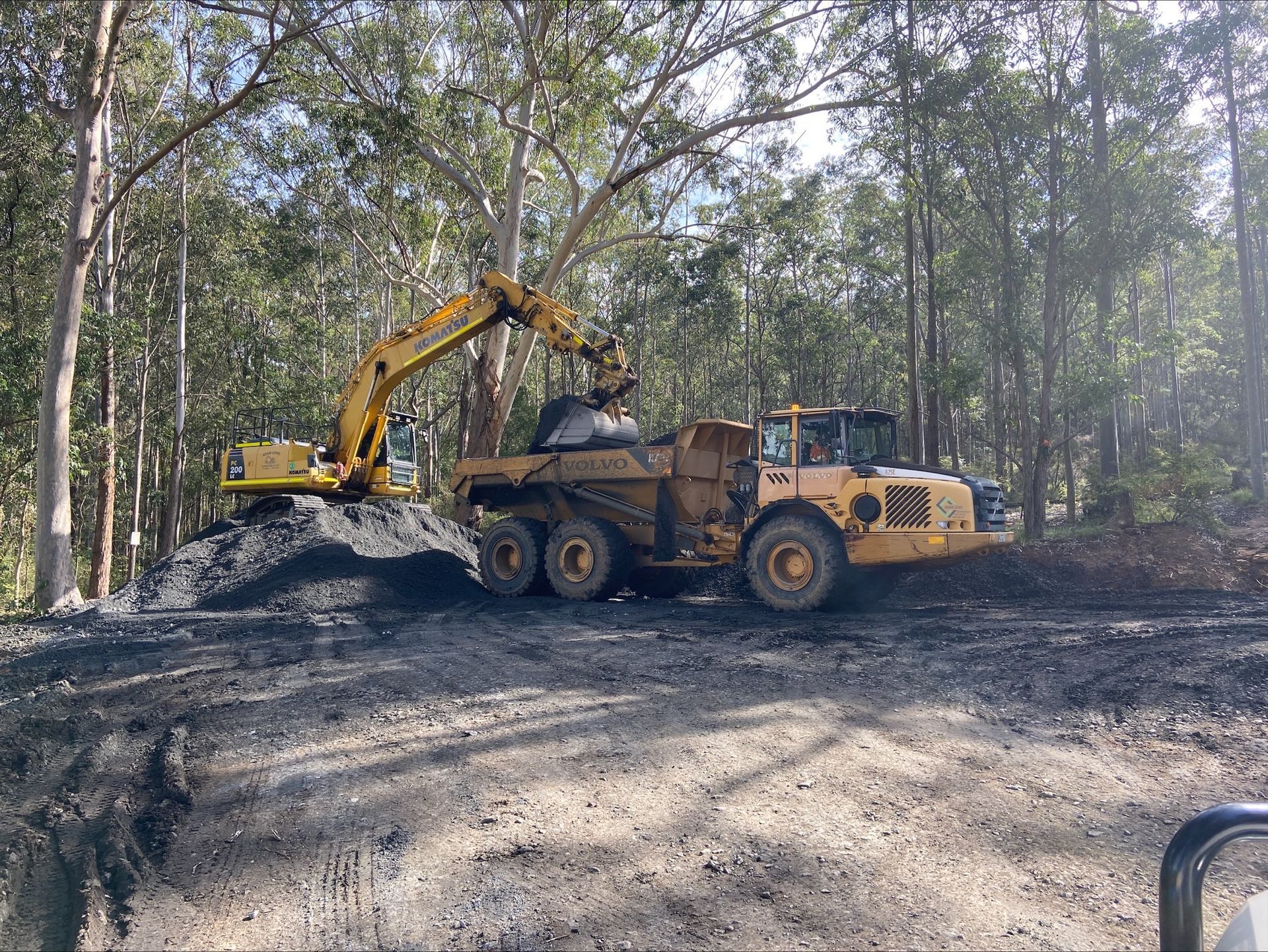 A yellow excavator is loading dirt into a dump truck. — Adam Lowe Earthmoving Pty Ltd in Somersby, NSW