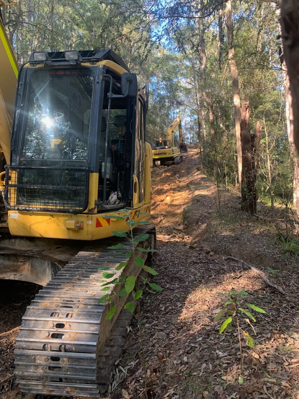 A yellow excavator is sitting in the middle of a forest. — Adam Lowe Earthmoving Pty Ltd in Somersby, NSW