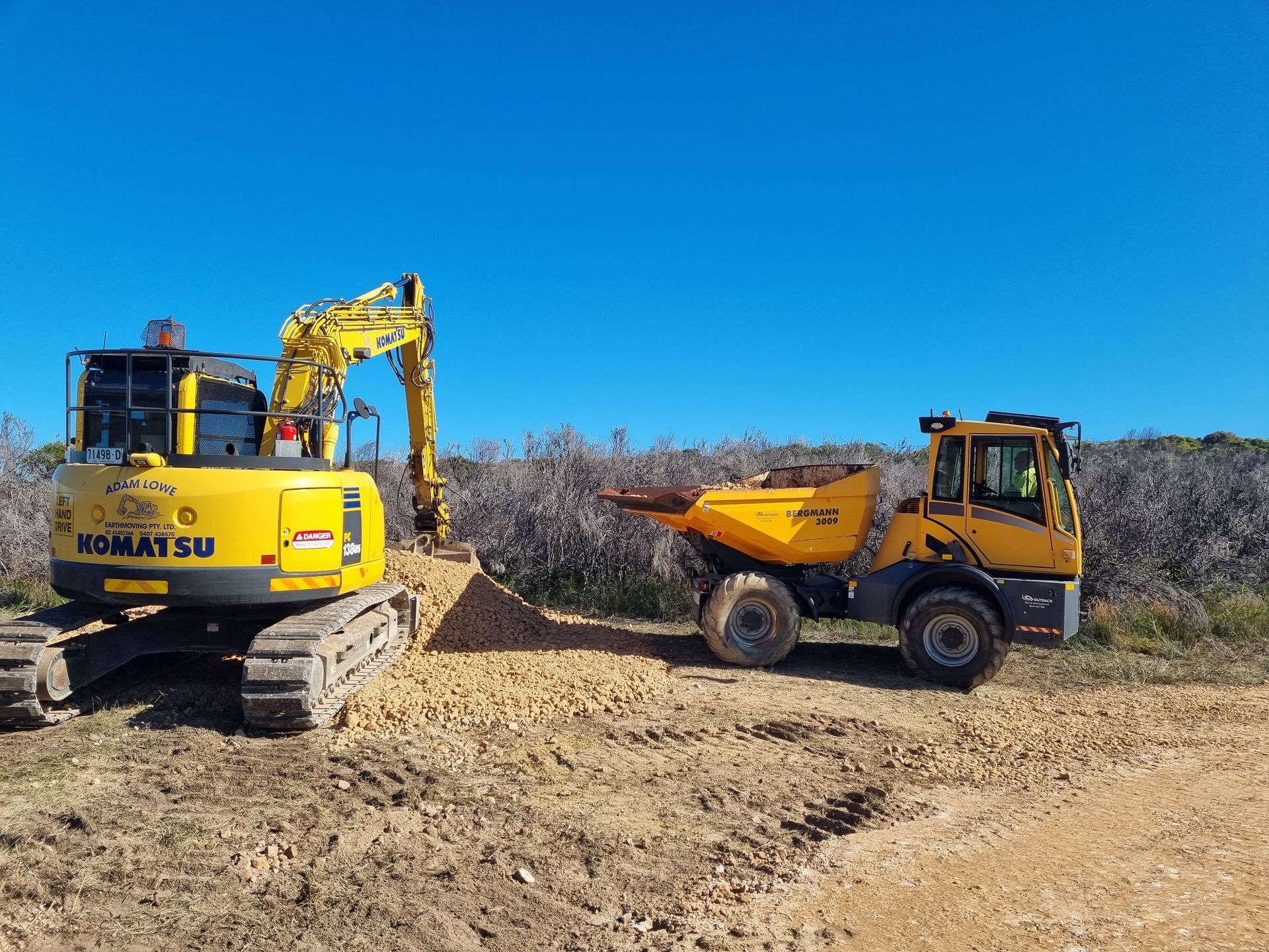 A yellow komatsu excavator is digging in the dirt next to a dump truck. — Adam Lowe Earthmoving Pty Ltd in Somersby, NSW