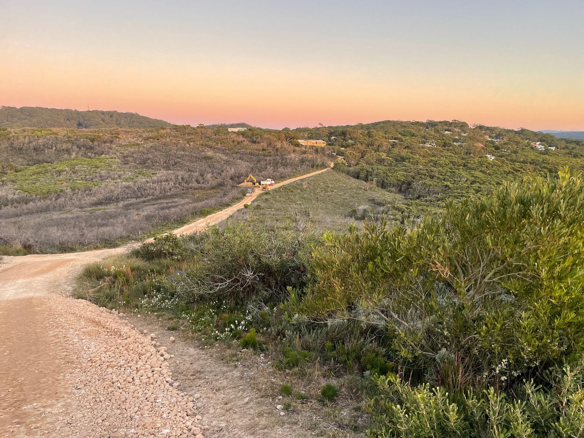A dirt road going through a lush green field at sunset. — Adam Lowe Earthmoving Pty Ltd in Somersby, NSW