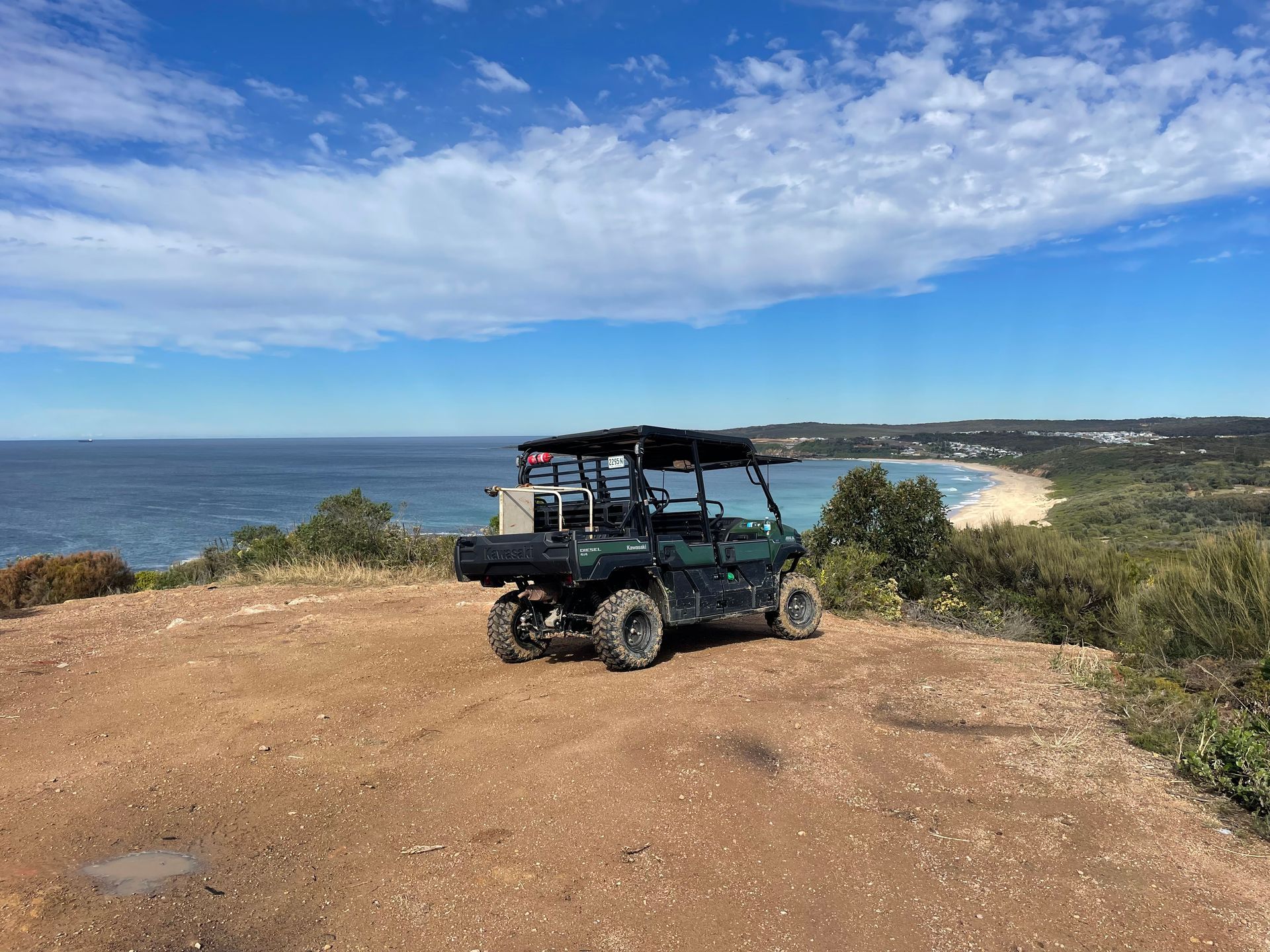 A green atv is parked on top of a dirt hill overlooking the ocean. — Adam Lowe Earthmoving Pty Ltd in Somersby, NSW